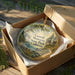 A decorative ornament in a wooden box, featuring a scenic landscape with a house and trees, with the text "Caswell Memorial State Park, California" printed on it.