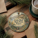 A decorative ornament with the text "Cedar Bluff State Park, Kansas" on it, surrounded by pine branches and a cup of coffee on a wooden surface.