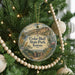 A round ornament hanging on a Christmas tree, featuring a scenic landscape with a mountain and a river.
