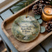 A decorative ornament featuring a scenic image of Chain O Lakes State Park, Indiana, with a candle and pine cones on a wooden tray.