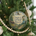 A round ornament on a Christmas tree, featuring a scenic landscape with a cabin and a plane flying overhead.