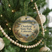 A round ornament hanging on a Christmas tree, featuring a scenic landscape with mountains, a lake, and a boat.