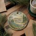 A circular ornament with a scenic landscape of Cheboygan State Park, Michigan, featuring pine trees, a lake, and mountains.