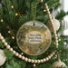 A round ornament hanging on a Christmas tree, featuring a scenic landscape with a winding path and a bird in flight.