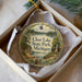 A decorative ornament in a box, featuring a scenic landscape with a lake, trees, and a cabin, with the text "Clear Lake State Park, Michigan" printed on it.
