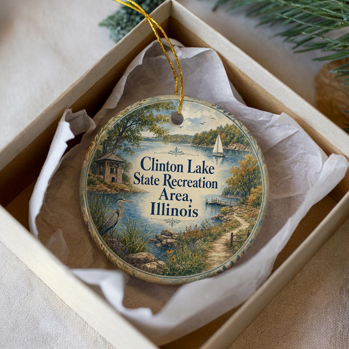 A decorative ornament in a white box, featuring a scenic landscape with a lake, a boat, and a bird.