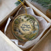 A decorative ornament in a box, featuring a scenic landscape with a waterfall and a castle in the background.