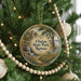 A round ornament hanging on a Christmas tree, featuring a scenic landscape with a waterfall and trees.