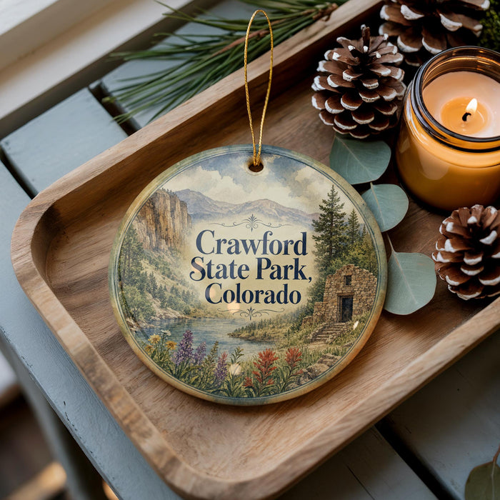 A decorative ornament featuring a scenic landscape of Crawford State Park, Colorado, with pine cones and a lit candle on a wooden tray.