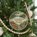 A round ornament hanging on a Christmas tree, featuring a scenic landscape with a waterfall and pine trees.