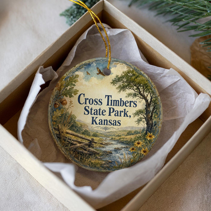 A decorative ornament in a white box, featuring a scenic landscape with a river, trees, and flowers.