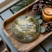 A wooden tray with a decorative ornament featuring a scenic landscape of Cross Timbers State Park, Kansas, along with pine cones and a lit candle.