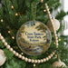 A round ornament hanging on a Christmas tree, featuring a scenic landscape with a river and trees.