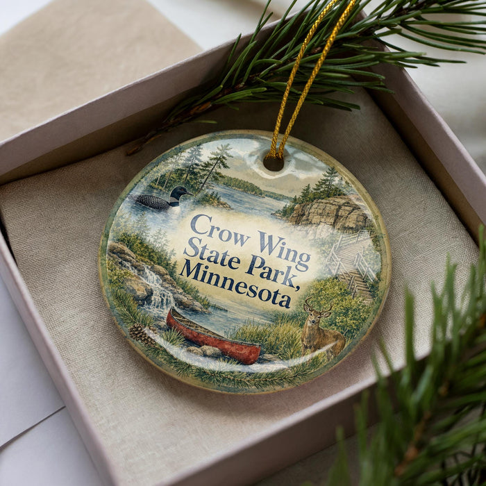 A decorative ornament in a box, featuring a scenic landscape with a lake, mountains, and wildlife.