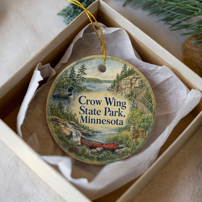 A decorative ornament in a box, featuring a scenic landscape with a lake, mountains, and wildlife.