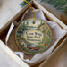 A decorative ornament in a box, featuring a scenic landscape with a lake, mountains, and wildlife.