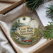 A decorative ornament with a scenic landscape of a lake, forest, and wildlife, including a duck and a deer, is displayed in a box.