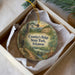 A decorative ornament in a box, featuring a scenic landscape with a river, mountains, and wildlife.