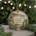 A round ornament featuring a scenic coastal landscape with a house, palm trees, and a surfboard, hanging in front of a blurred background with Christmas lights.