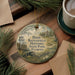 A round ornament with a painting of a historical site, specifically Dade Battlefield Historic State Park, Florida, hanging on a wooden surface.