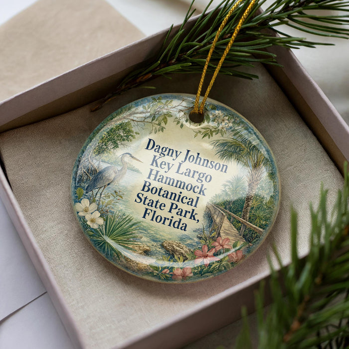 A decorative ornament with a tropical scene, featuring a bird, palm trees, and flowers, is displayed in a box.