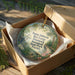 A decorative ornament in a cardboard box, featuring a tropical scene with a bird and flowers.