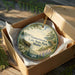 A decorative ornament in a wooden box, featuring a scenic landscape with pine trees, a lake, and a boat, along with the text "Darmiscotta Lake State Park, Maine".