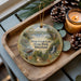 A decorative ornament featuring a scenic view of Deep Creek Lake State Park, Maryland, with pine cones and a lit candle on a wooden tray.