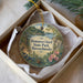 A decorative ornament in a box, featuring a scenic landscape with a lake, trees, and flowers.