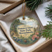 A decorative ornament with a landscape scene and text, placed in a box with pine branches.