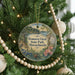 A round ornament hanging on a Christmas tree, featuring a scenic landscape with a lake and trees.