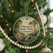 A round ornament hanging on a Christmas tree, featuring a scenic landscape with a river and trees.
