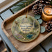 A decorative ornament featuring a scenic image of Dixon Springs State Park, Illinois, with a candle and pine cones on a wooden tray.