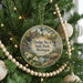 A round ornament hanging on a Christmas tree, featuring a scenic landscape with a watermill and flowers.