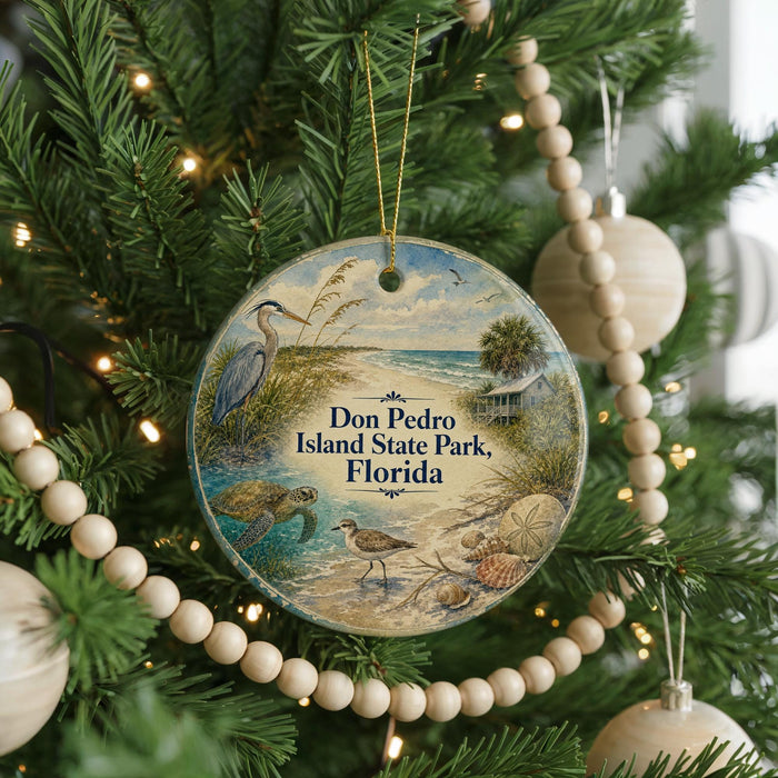 A round ornament hanging on a Christmas tree, featuring a beach scene with a bird, turtle, and palm tree.