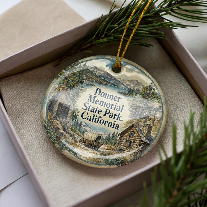 A decorative ornament in a box, featuring a scenic landscape with mountains, a cabin, and a wagon, along with the text "Donner Memorial State Park, California".
