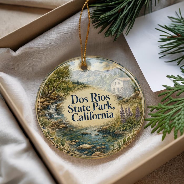 A decorative ornament with a scenic landscape of a river, mountains, and a house, hanging from a string.