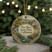 A round ornament with a scenic landscape of a river, mountains, and a building, hanging from a string.