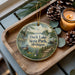 A wooden tray with a decorative ornament featuring a scenic image of Duck Lake State Park, Michigan, along with pine cones and a lit candle.