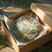 An ornament in a wooden box, featuring a scenic landscape with a windmill, trees, and a house, with the text "Dudley Farm Historic State Park, Florida" printed on it.