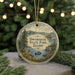 A round ornament with a scenic landscape featuring a lake, mountains, and a deer, hanging from a string.
