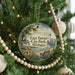 A round ornament hanging on a Christmas tree, featuring a scenic view of East Tawas City Park in Michigan.
