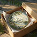 A decorative ornament in a box, featuring a scenic view of East Tawas City Park in Michigan.