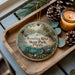 A decorative ornament featuring a scenic image of the Econfina River State Park in Florida, with pine cones and a lit candle on a wooden tray.