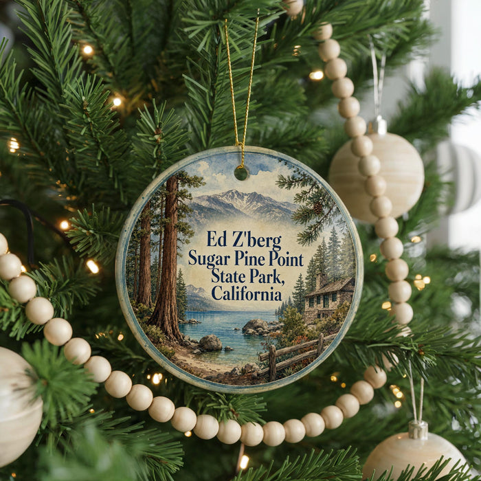 A round ornament hanging on a Christmas tree, featuring a scenic landscape with mountains, pine trees, and a lake.