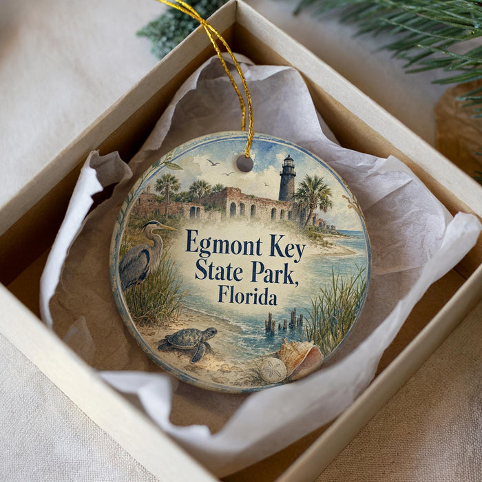 A decorative ornament in a box, featuring a lighthouse and a beach scene, with the text "Egmont Key State Park, Florida" printed on it.