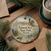 A decorative ornament featuring a lighthouse and palm trees, with the text "Egmont Key State Park, Florida" displayed on it. The ornament is placed on a wooden surface, surrounded by pine branches and a cup of coffee.