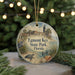 A round ornament with a lighthouse and beach scene, featuring a bird and turtle, hangs in front of a Christmas tree with lights.