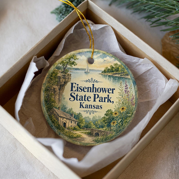 A decorative ornament in a box, featuring a scenic landscape with a house, trees, and a body of water.