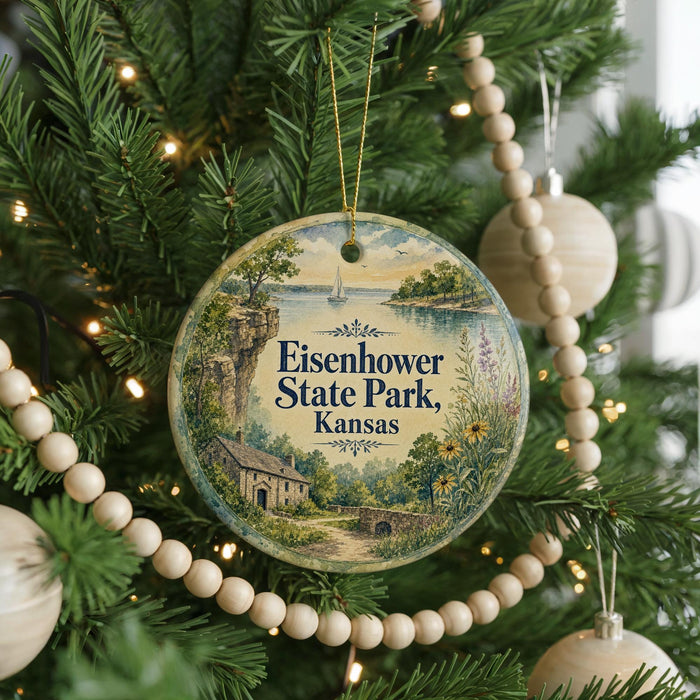 A round ornament hanging on a Christmas tree, featuring a scenic landscape with a house, trees, and a body of water.
